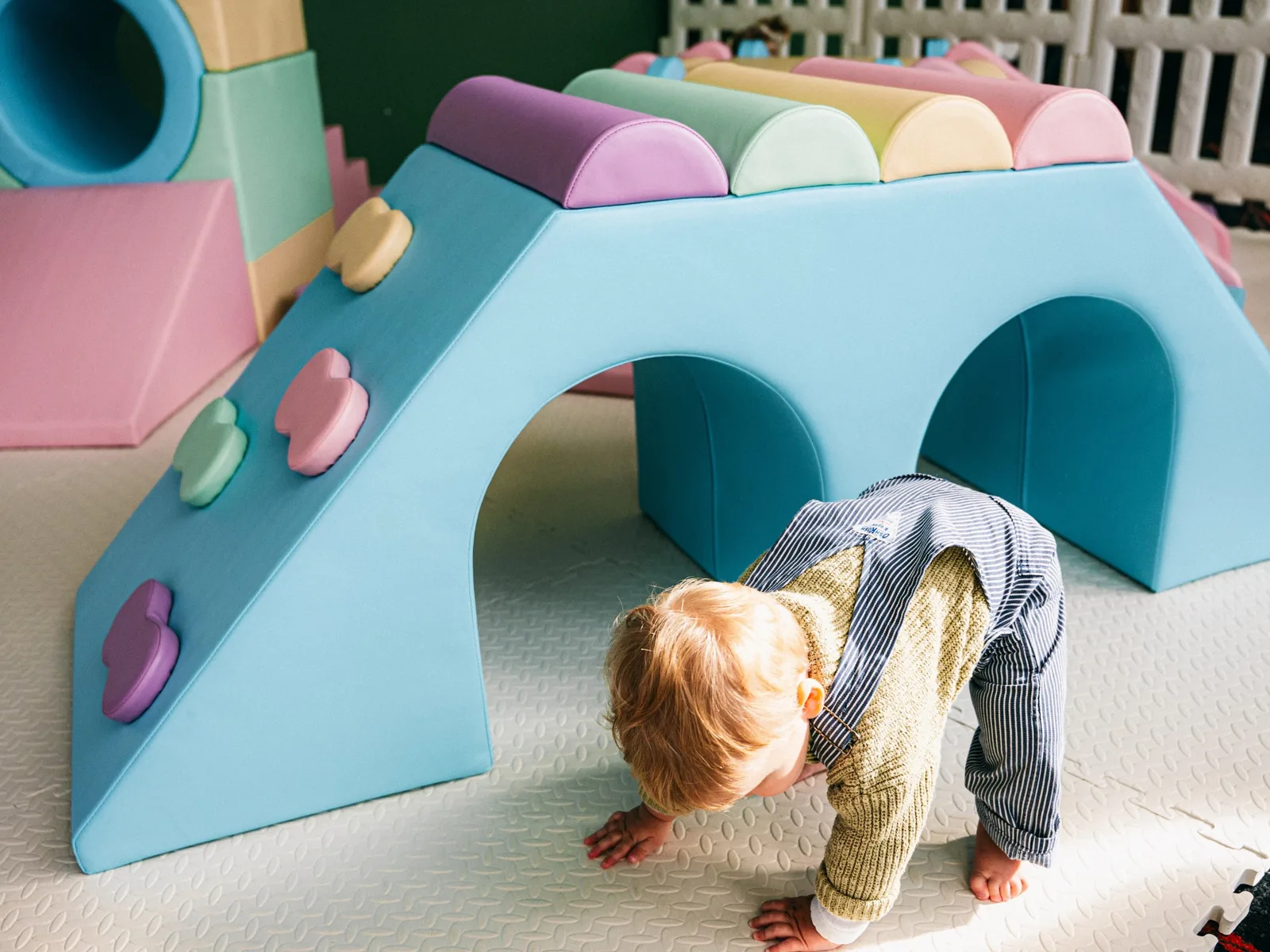 A toddler crawling under a pastel soft play arch inside a Joyful Little Spaces set up