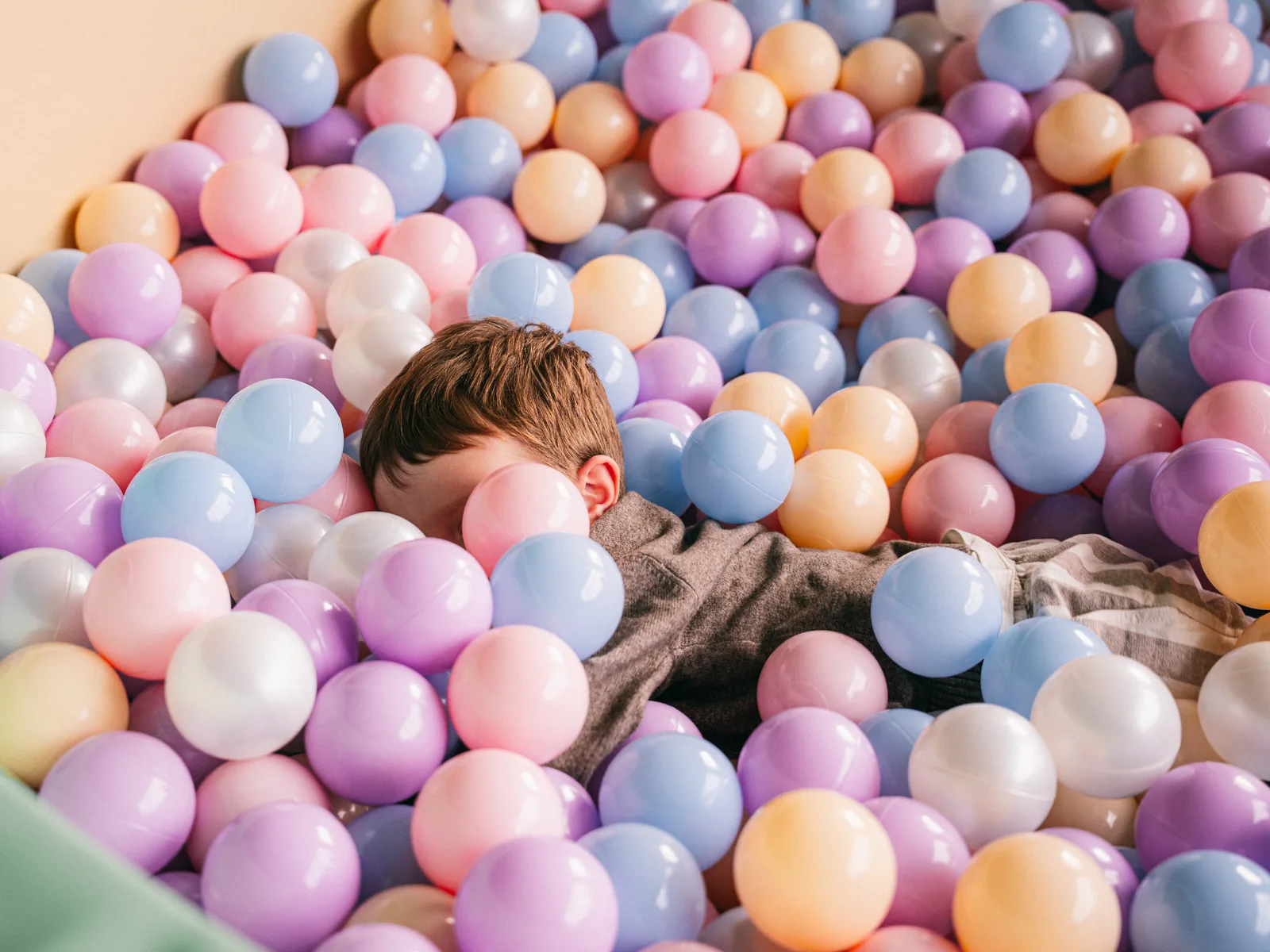 A child playing in a pastel ball pit filled with soft play balls