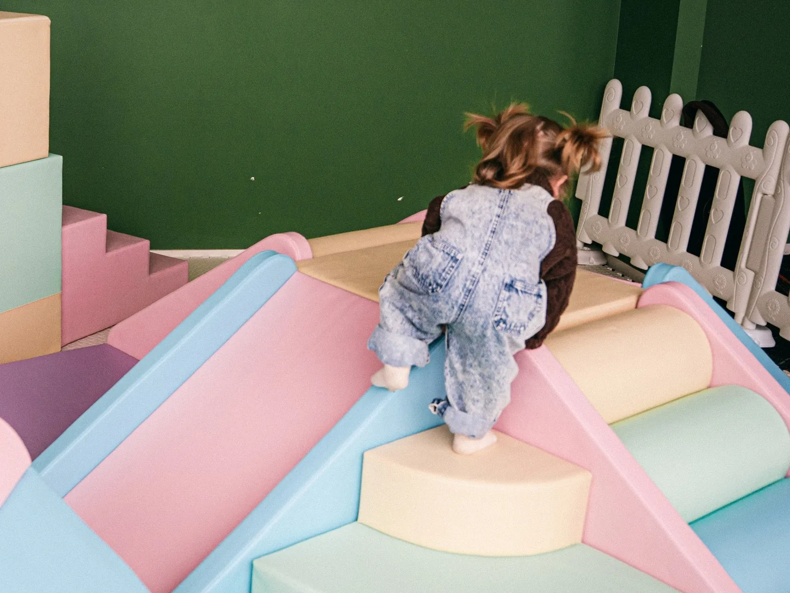 A toddler climbing the pastel soft play steps beside a slide